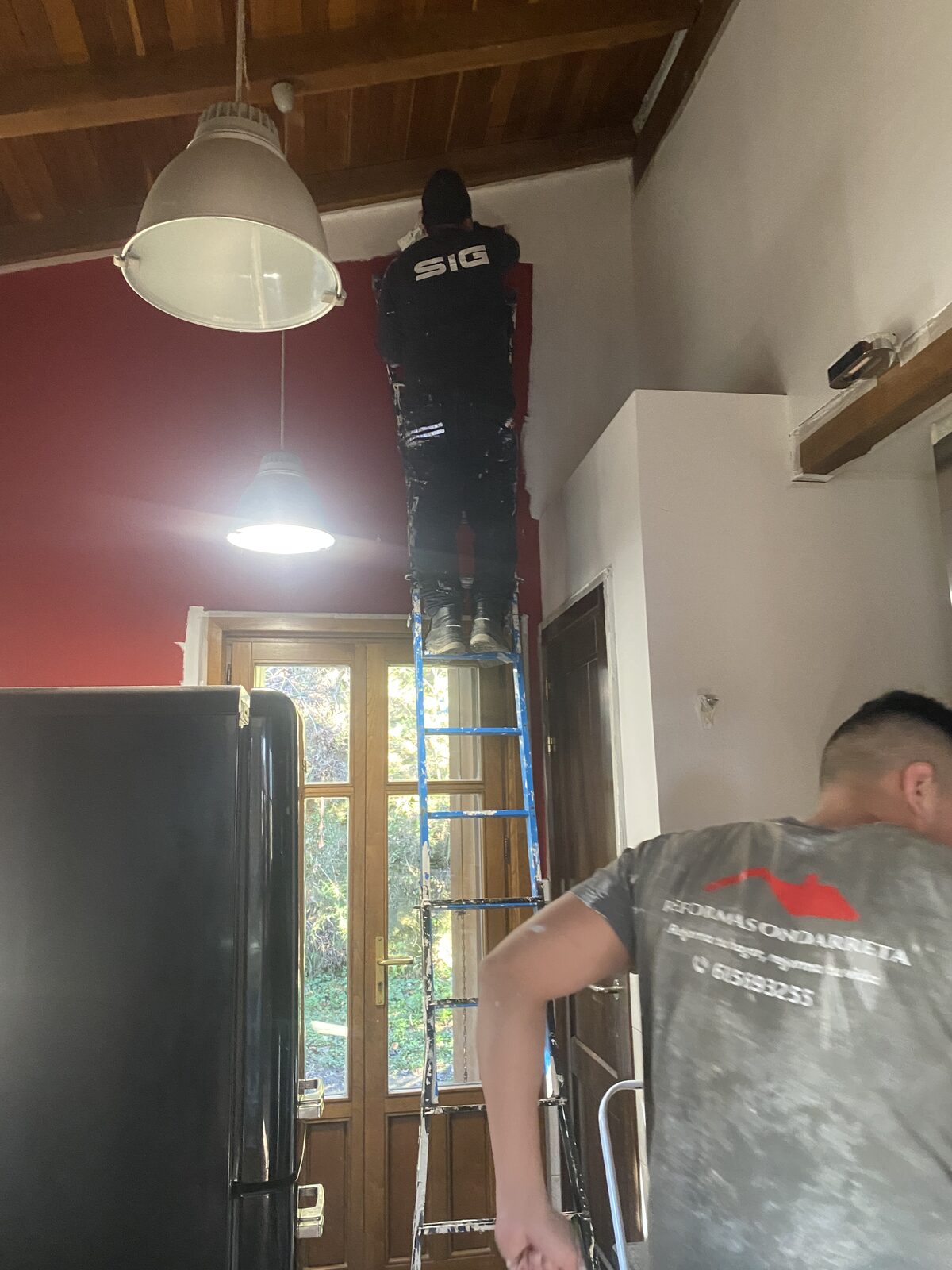 Pintor trabajando en altura sobre escalera en pared roja